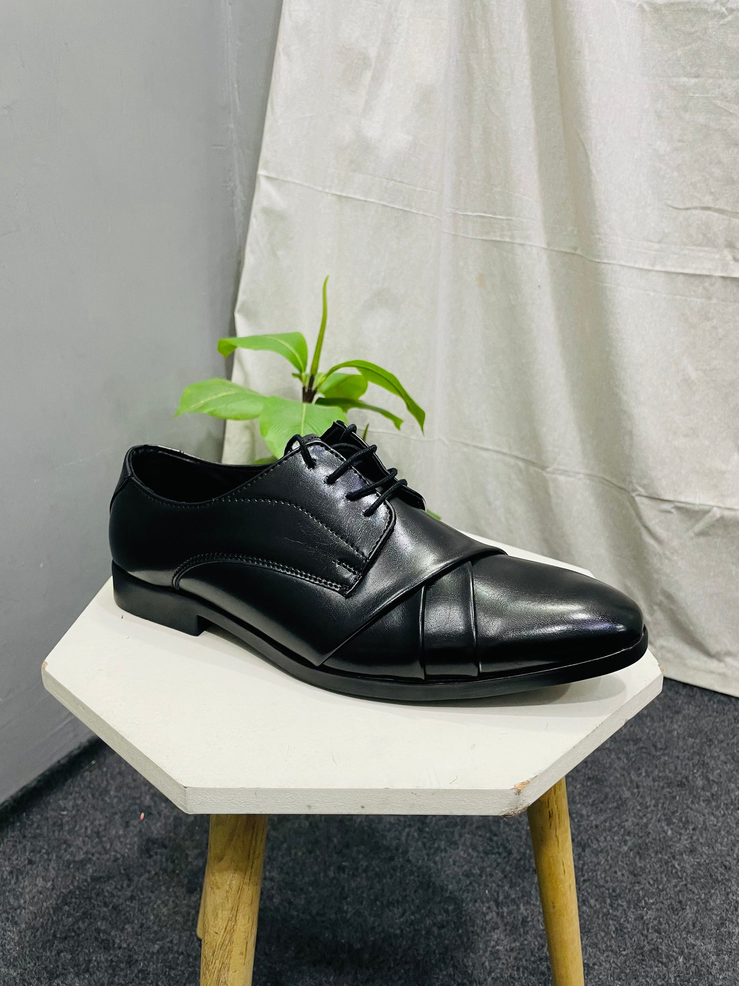 Black leather dress shoe placed on a white platform with a green plant in the background